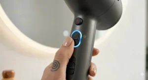 A detailed close-up of a hand actively pressing the textured black cool shot button on a dark grey hair dryer to set a hairstyle.