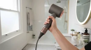 A close-up of a hand gripping the contoured, ergonomic handle of the hairdryer, with the flexible swivel cord connection clearly visible at the base.