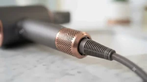 A detailed macro close-up of the robust 360-degree swivel cord mechanism at the base of the graphite and rose-gold hairdryer handle, showing its engineering.