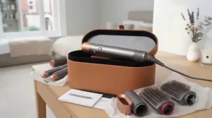 The unboxed grey and rose gold multi-styler wand resting on its opened tan presentation case, surrounded by attachments and paper wrapping on a vanity.