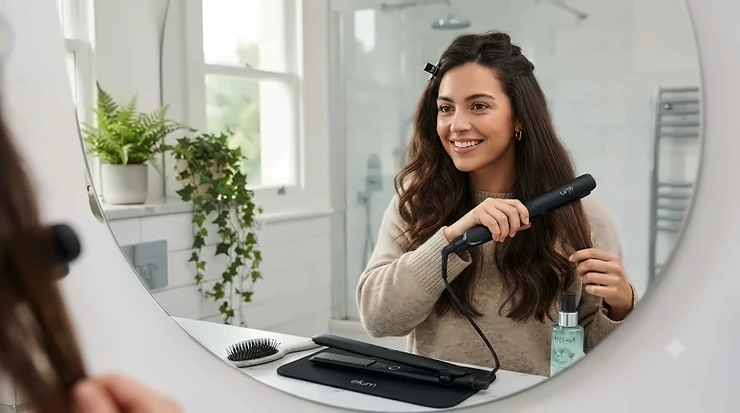 A person with thick, wavy hair smiling while using ceramic straighteners in a modern British bathroom. ceramic straighteners for thick hair