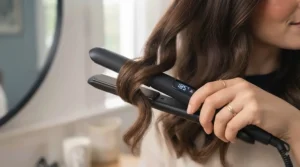 The professional hair straightener resting safely on a grey silicone heat mat on a dressing table, featuring an automatic shut-off indicator light.