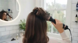 Back view of someone lifting hair sections at the crown for extra volume using a 2 in 1 hair dryer brush.
