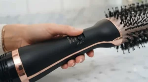 Hand adjusting the cool, low, and high-temperature switch on the handle of a 2 in 1 hair dryer brush.