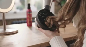 Hair dryer fitted with a curl diffuser attachment being used to define natural waves.