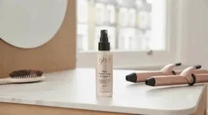 A bottle of professional heat defence spray positioned next to styling tools to protect hair from heat damage before curling.